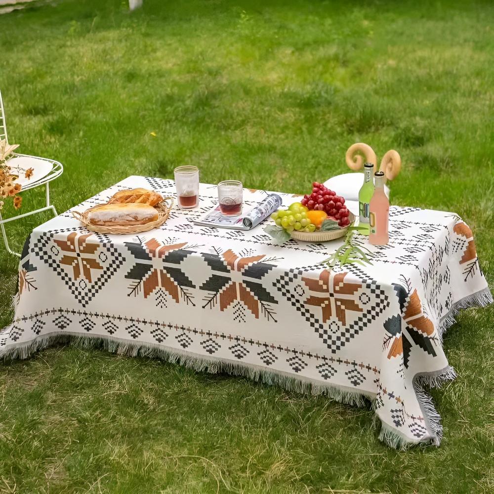 Nomad Oasis picnic blanket with Moroccan boho pattern draped over an outdoor table on green grass, set with refreshing drinks, bread, and fruit, ideal for a stylish outdoor meal.