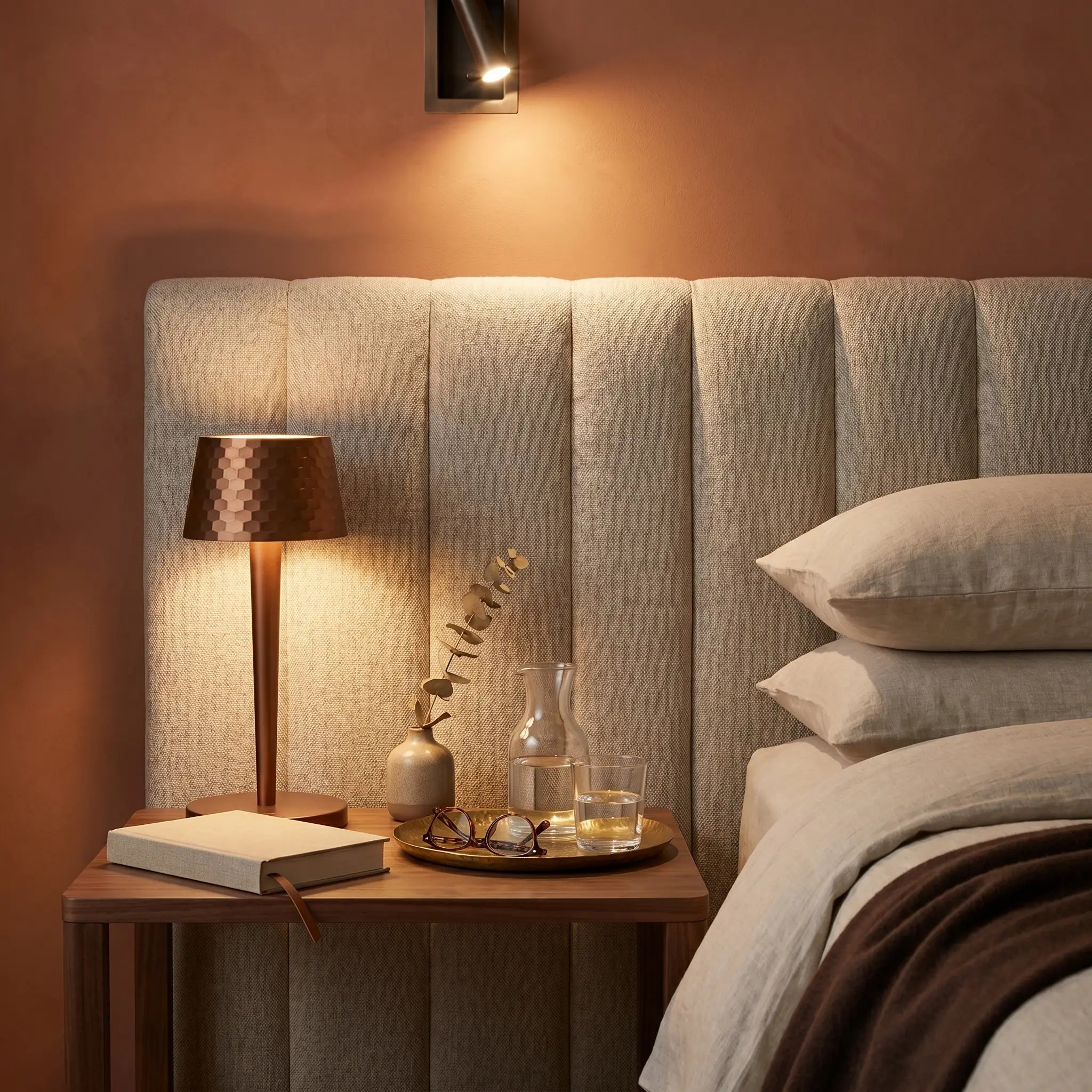 Aluminum touch dimmable USB rechargeable LED bedside lamp at three-quarter angle in brushed aluminum lit on hotel bedside with terracotta wall