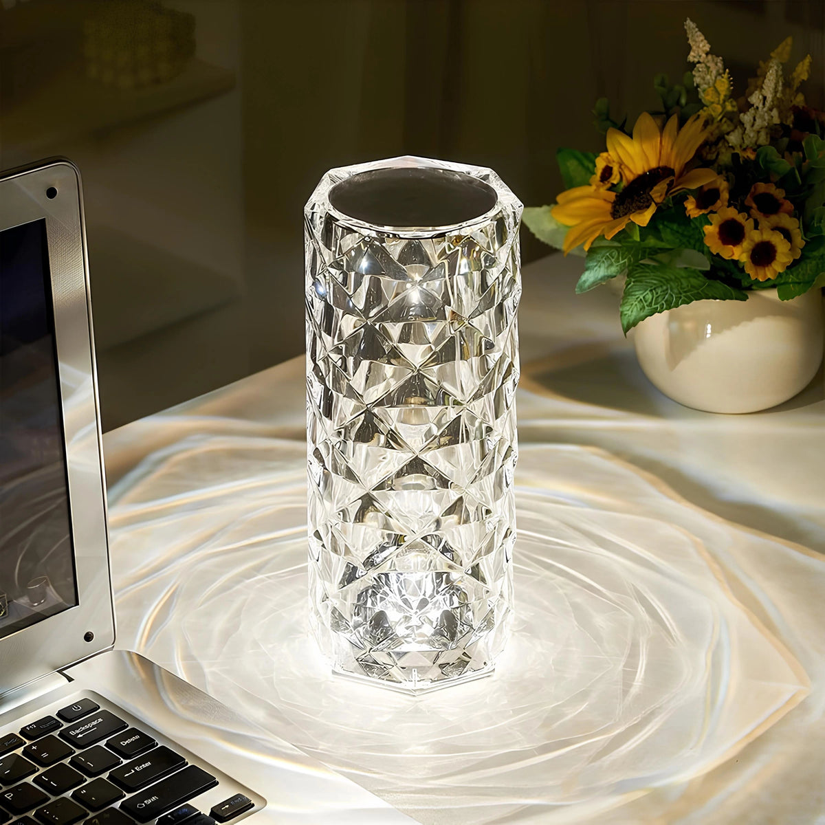 Radiant Aura Crystal Table Lamp with Touch Control, illuminated on a white tablecloth next to a laptop and a vase of sunflowers, showcasing its elegant design and ambient light.