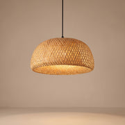 Handwoven bamboo dome pendant lamp shade lit with a warm glow on a beige studio background