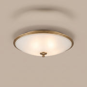 Orren pot-lid style frosted glass flush mount with gilded rim, lit, studio view