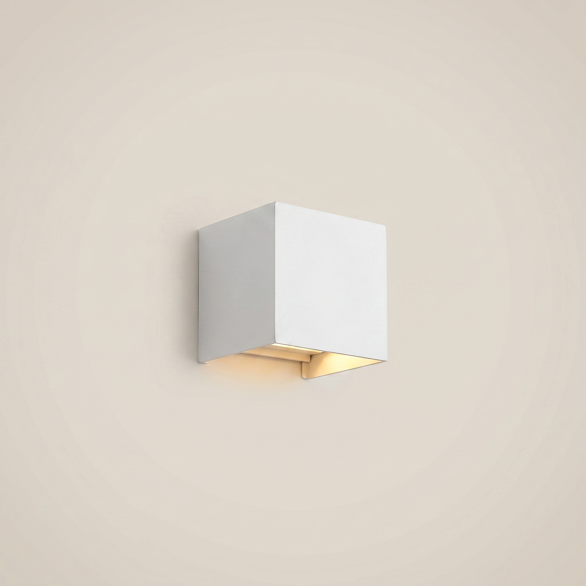 Eye-level wide shot of black aluminum square outdoor wall sconce lit on courtyard wall showing warm white dimmable glow