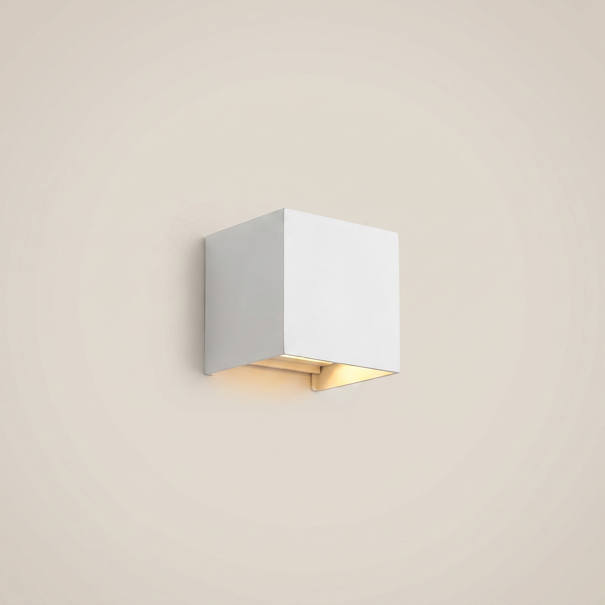 Eye-level wide shot of black aluminum square outdoor wall sconce lit on courtyard wall showing warm white dimmable glow