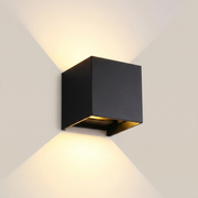 Black aluminum square outdoor wall sconce shown front view lit in ambient room lighting with adjustable light angle visible