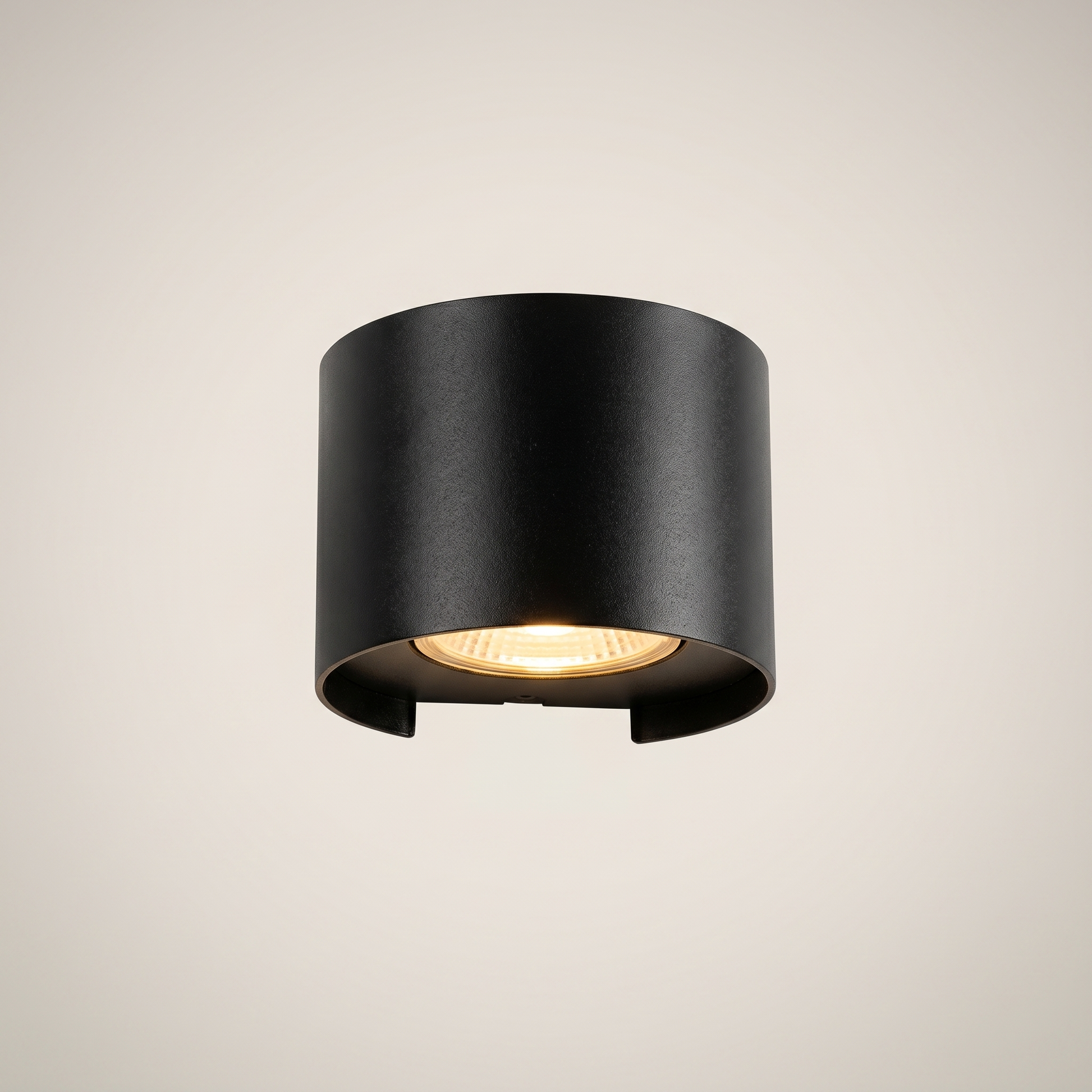 Three-quarter angle of black aluminum square outdoor wall sconce lit on exterior wall at night with warm white dimmed light