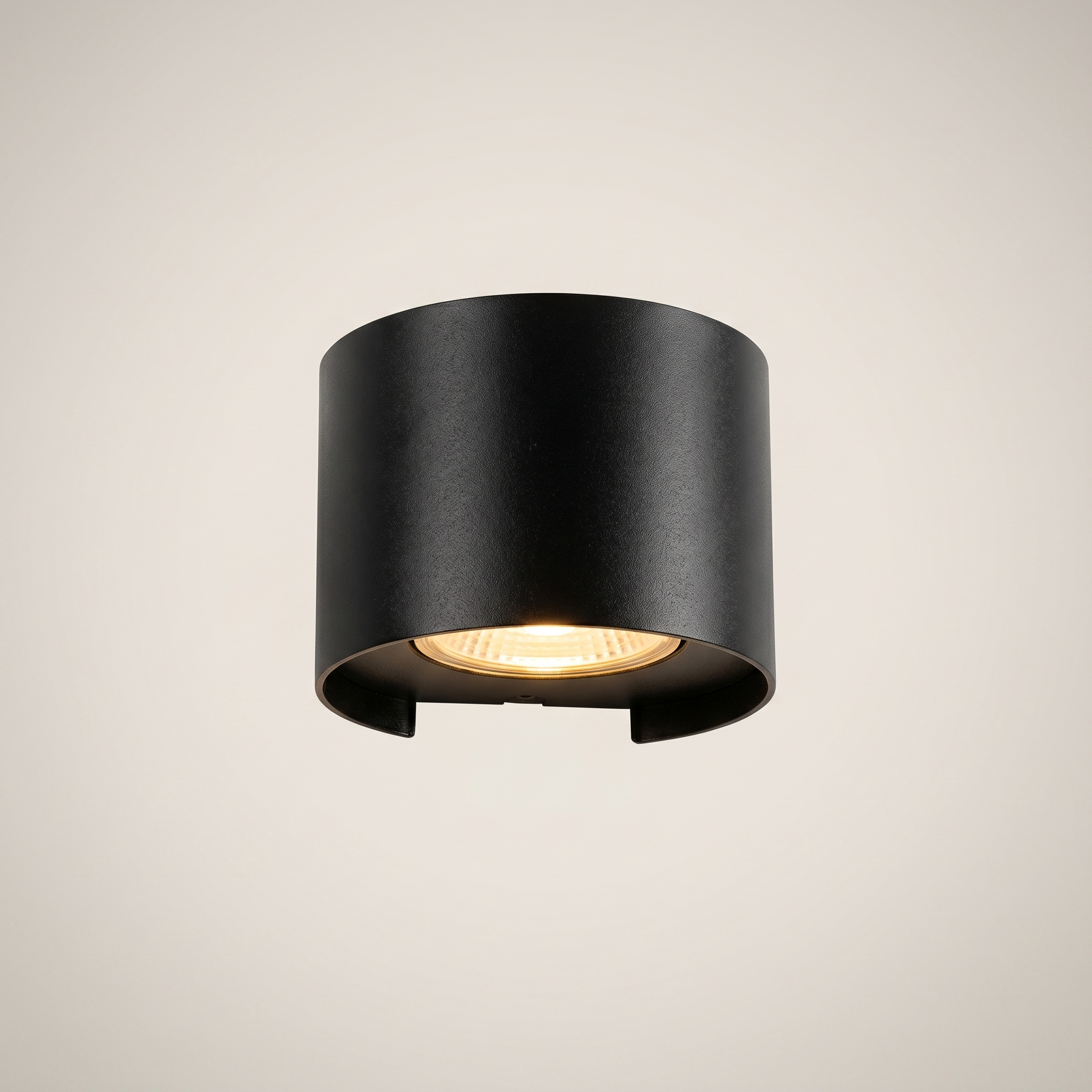 Three-quarter angle of black aluminum square outdoor wall sconce lit on exterior wall at night with warm white dimmed light