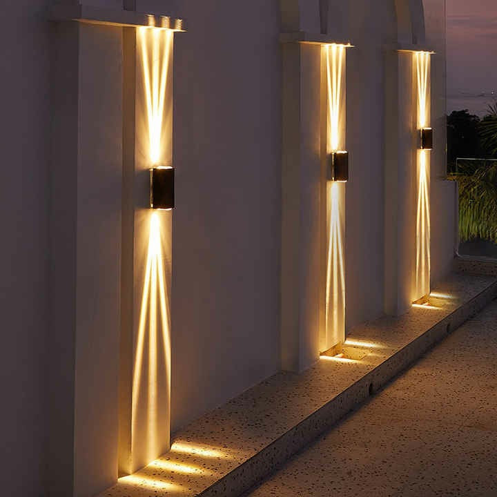 Close-up of black aluminum three-beam LED wall sconce lit with cool white light in outdoor corridor showing die-cast aluminum