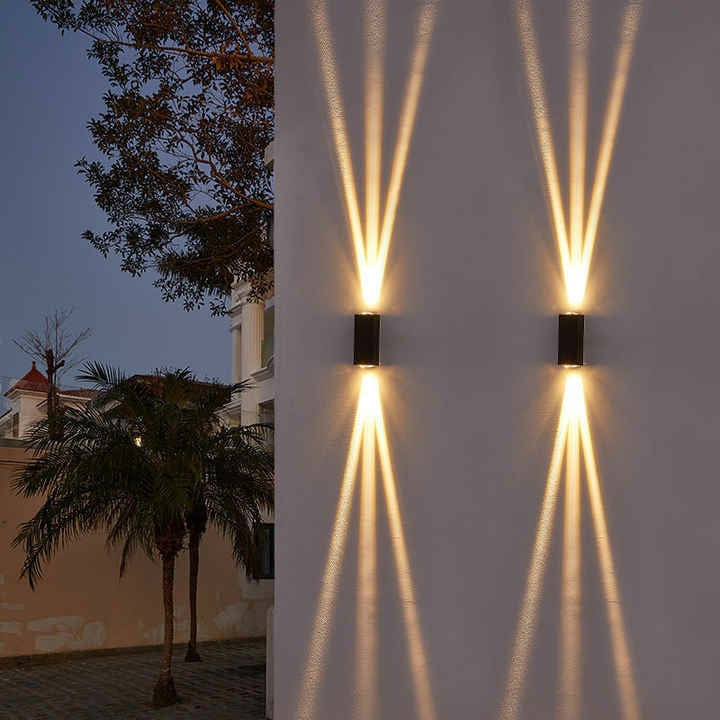 Eye-level wide shot of black aluminum three-beam LED wall sconce lit with cool white light on outdoor villa wall mounted