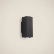 Black aluminum three-beam LED wall sconce at three-quarter angle switched off in outdoor corridor highlighting die-cast aluminum