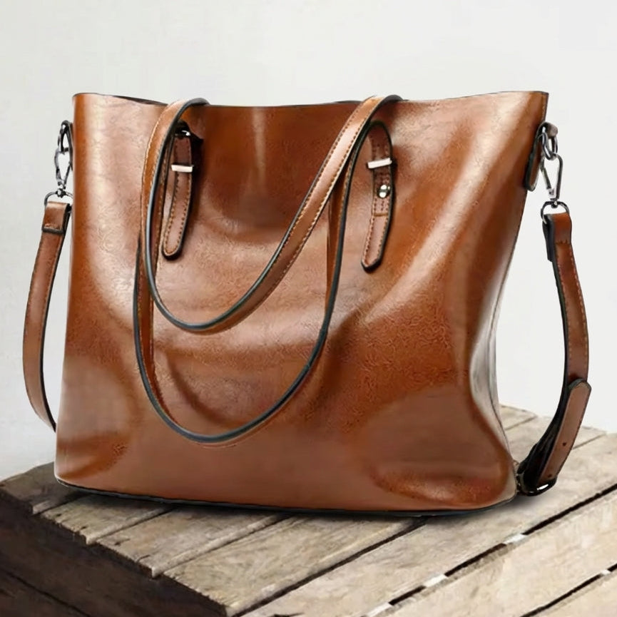 Elysian Voyage genuine leather shoulder bag in brown, featuring elegant hardware, dual top handles, and a detachable strap, displayed on a rustic wooden surface. Perfect for everyday use.