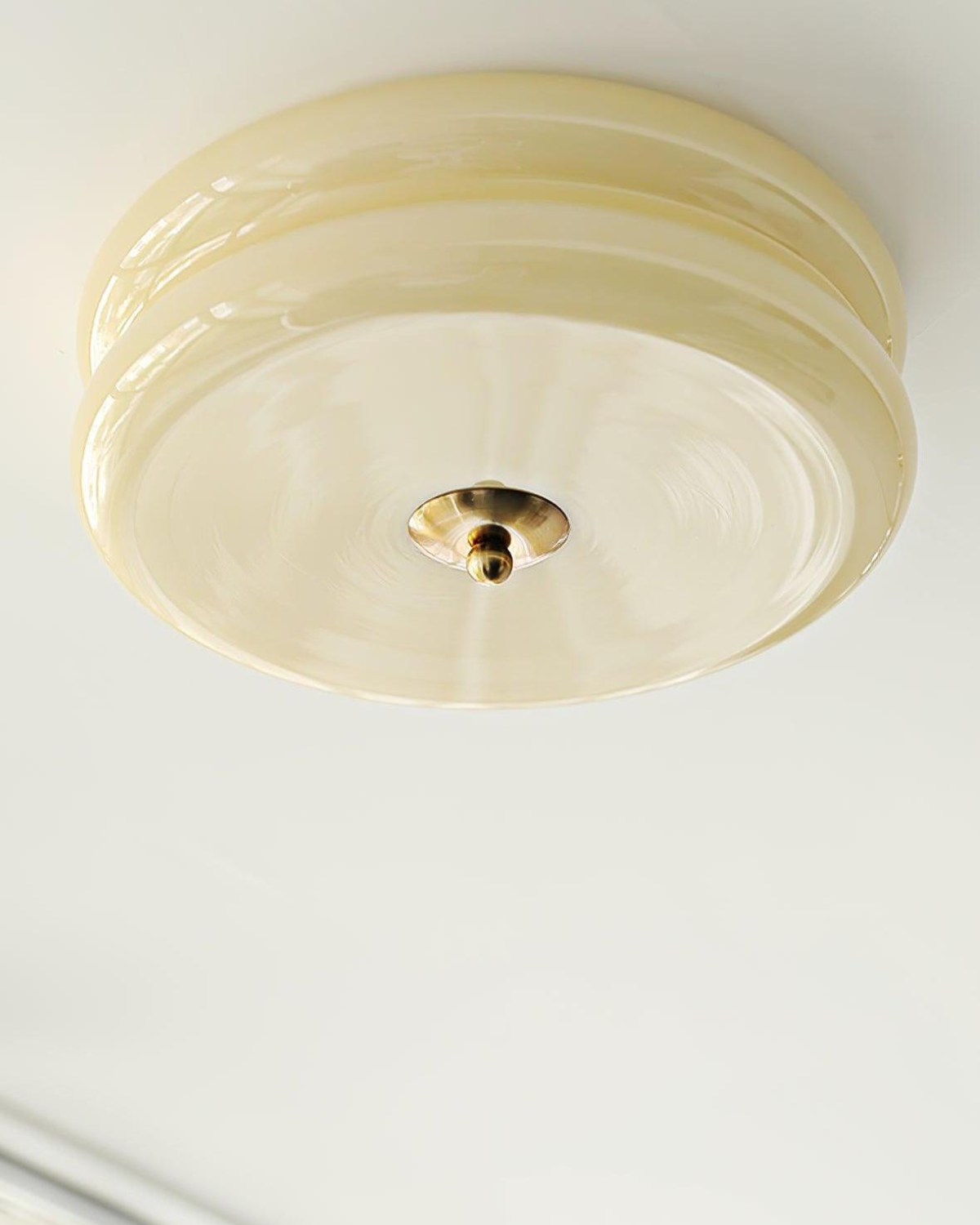 Close-up of the Époque glass pendant lamp with a beige glass shade and gold finish central knob, mounted on a ceiling.