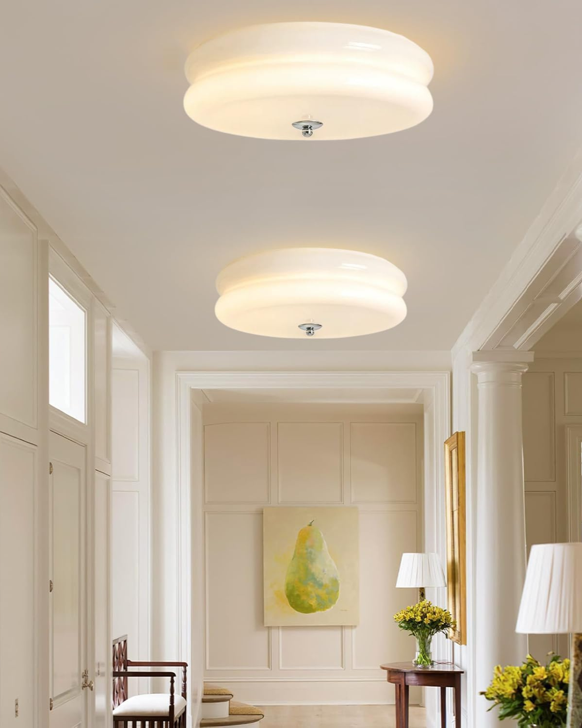 Two Époque glass pendant lamps with brass finish illuminating a stylish hallway, featuring a large pear painting, a wooden bench, and decorative elements.