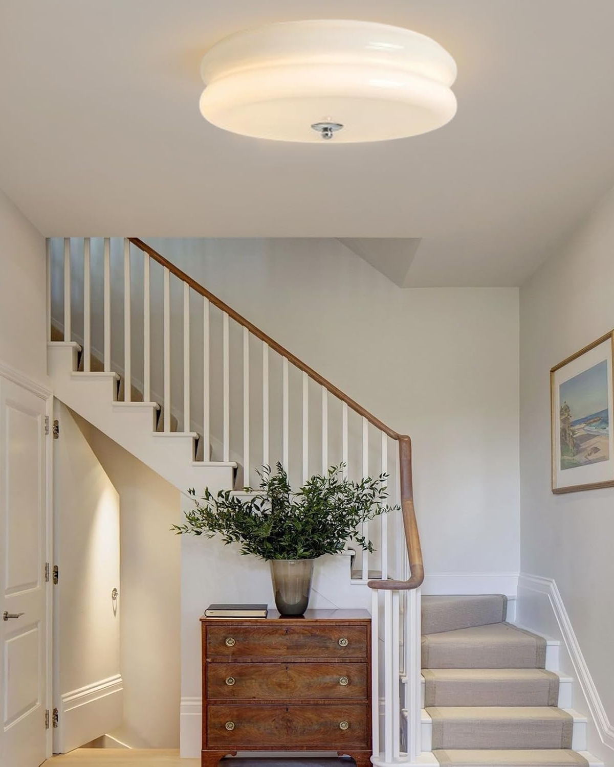 Époque glass pendant lamp with brass finish, illuminated in a hallway above a wooden dresser with a plant, beside a staircase.