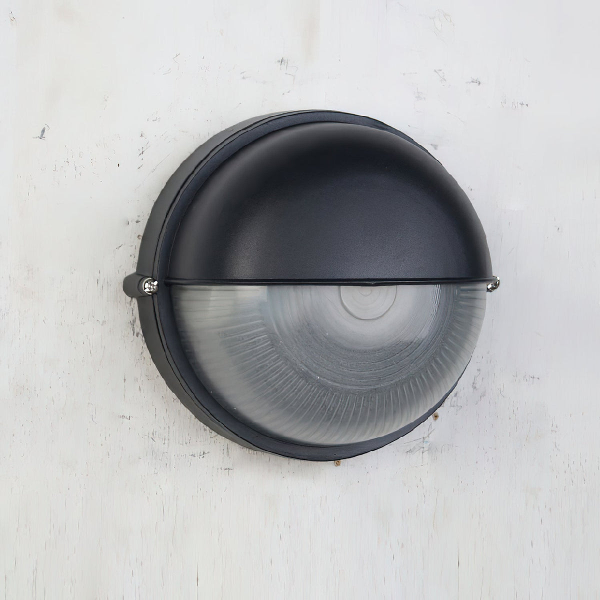 Vintage outdoor wall sconce in a black half-round dome design with ribbed glass, shown unlit on a light wooden background.