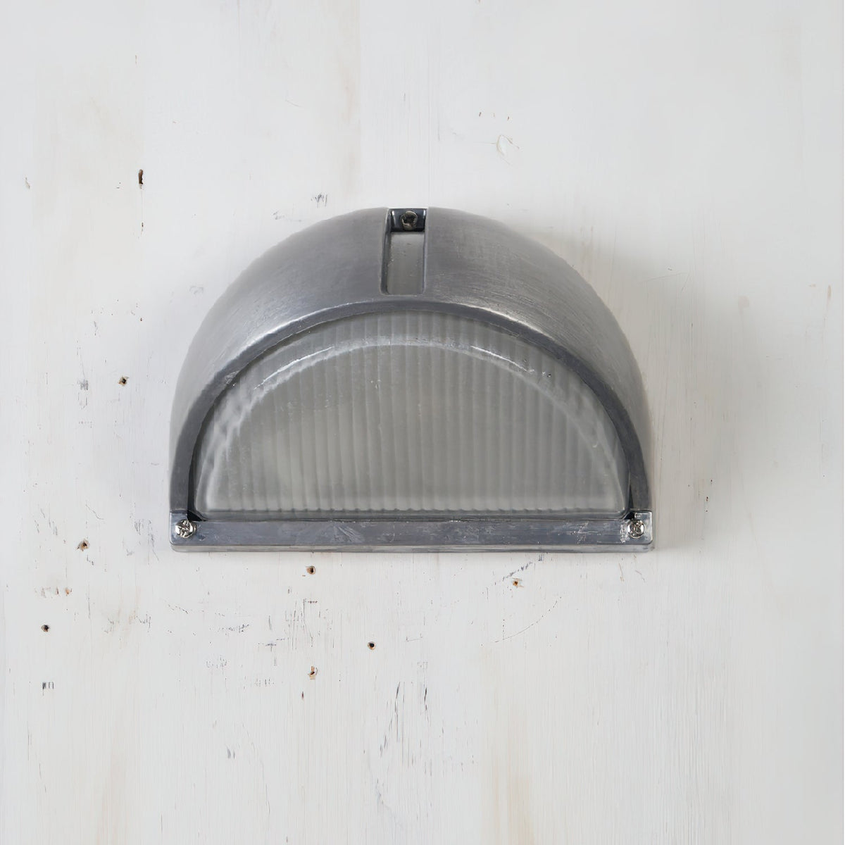 Vintage outdoor glass sconce wall lamp, half-dome silver metal frame with clear ribbed glass, mounted on a white wall.