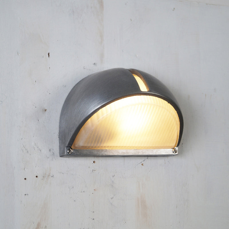 Fenwick vintage outdoor glass sconce wall lamp, half-dome design with gray metal frame and frosted glass, illuminated, mounted on a light wall.