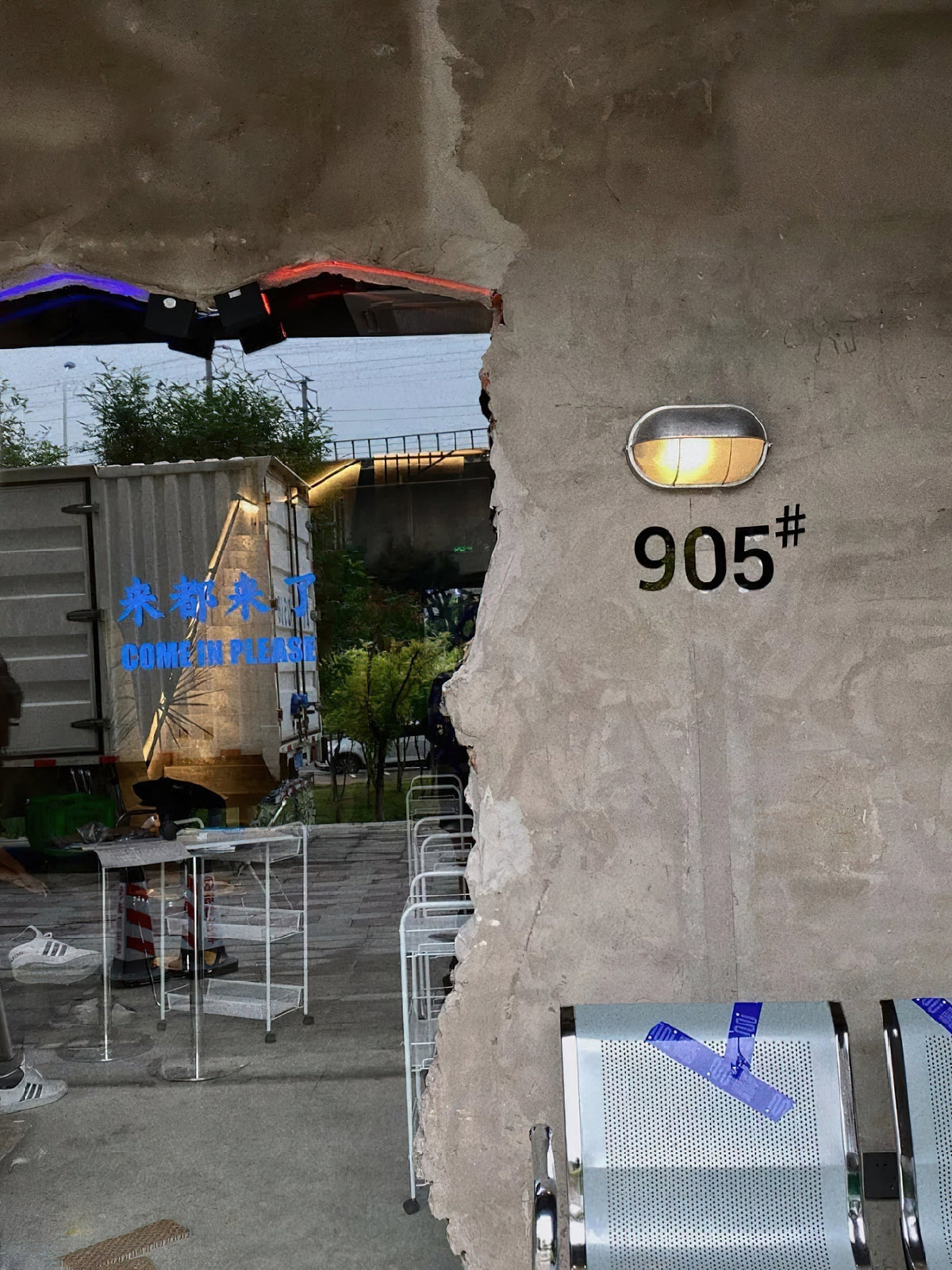 Vintage outdoor glass sconce wall lamp with metal frame and clear glass, illuminated on a rough concrete wall next to the number 905.