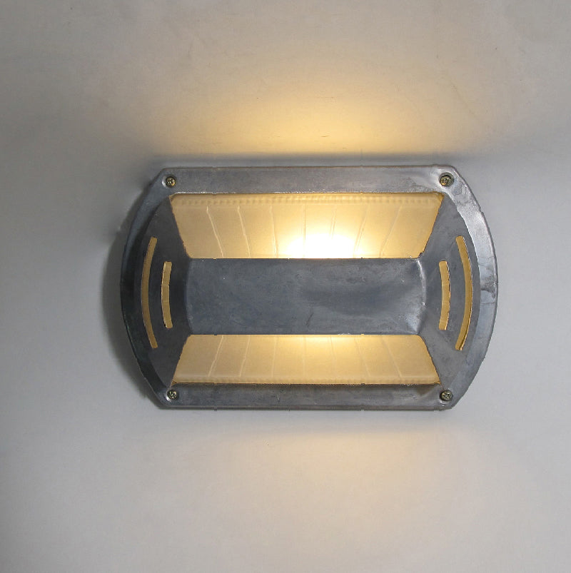 Fenwick vintage outdoor glass sconce wall lamp, oval industrial style metal frame with two clear ribbed glass sections separated by a central metal bar, illuminated on a light wall.