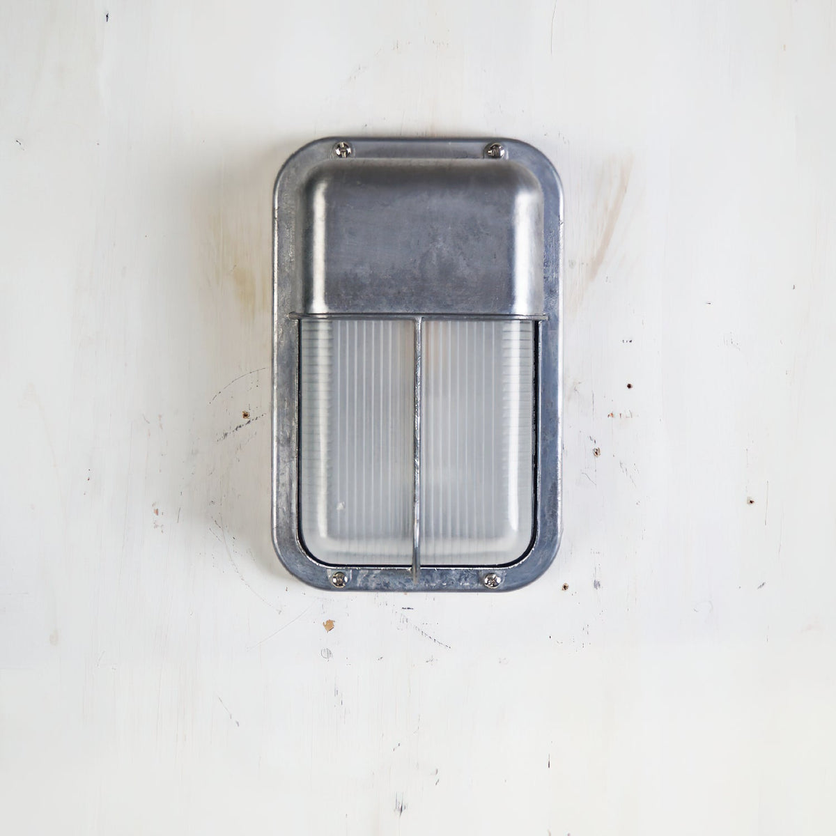 Vintage outdoor glass sconce wall lamp, rectangular silver metal frame with clear ribbed glass, mounted on a white wall.