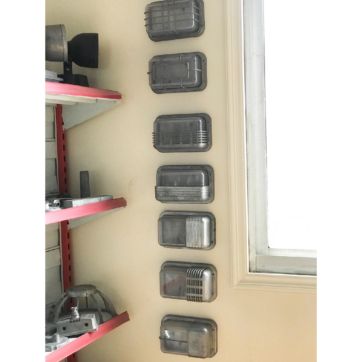 Seven different models of Fenwick vintage outdoor glass sconce wall lamps with metal frames and clear glass, mounted vertically on a light-colored wall, showcasing various rectangular designs.