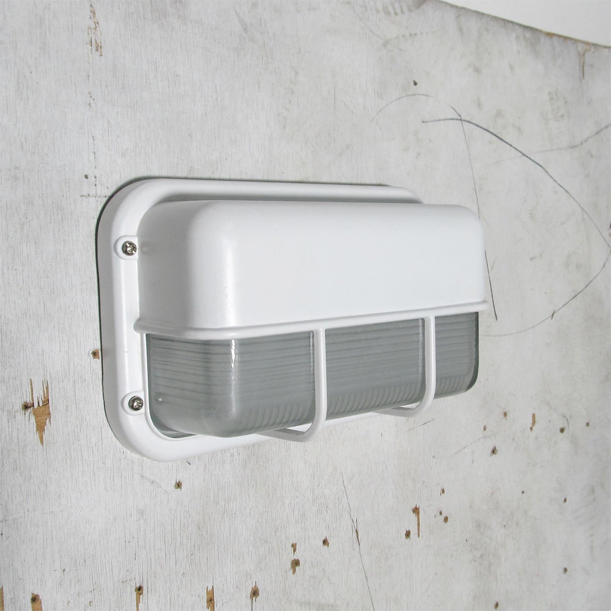 Fenwick vintage outdoor glass sconce wall lamp with a white metal frame and clear ribbed glass diffuser, shown off on a distressed white wall.