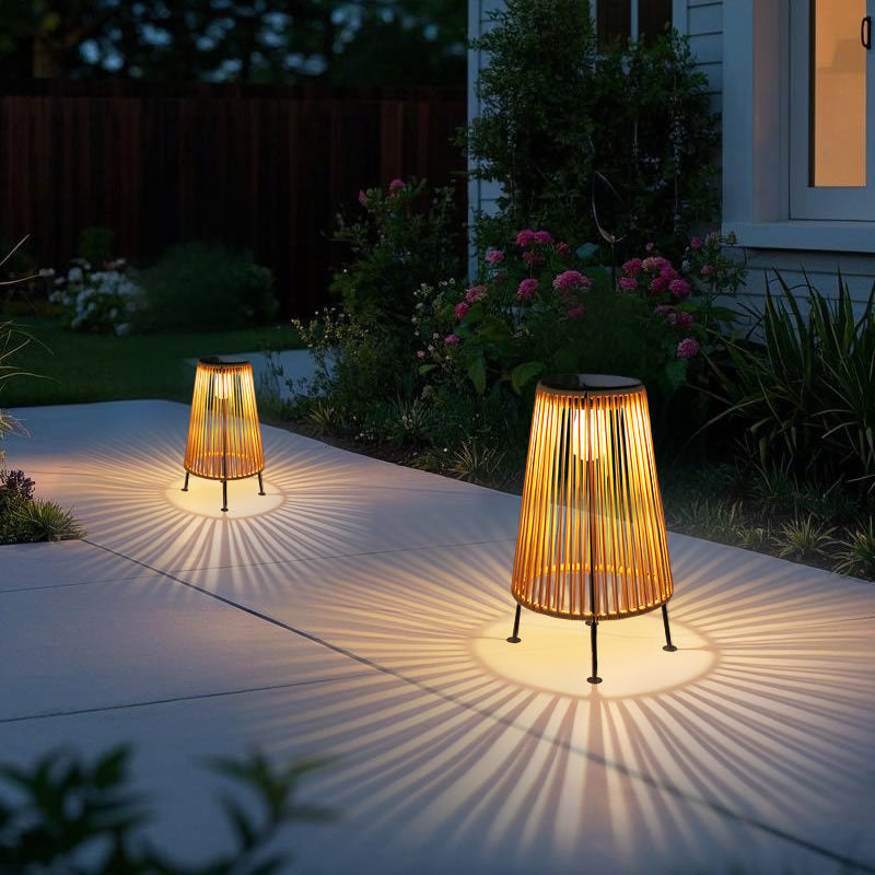 Ambient room three-quarter view of handwoven rattan geometric solar LED tripod outdoor lantern in natural tan with warm glow on lawn