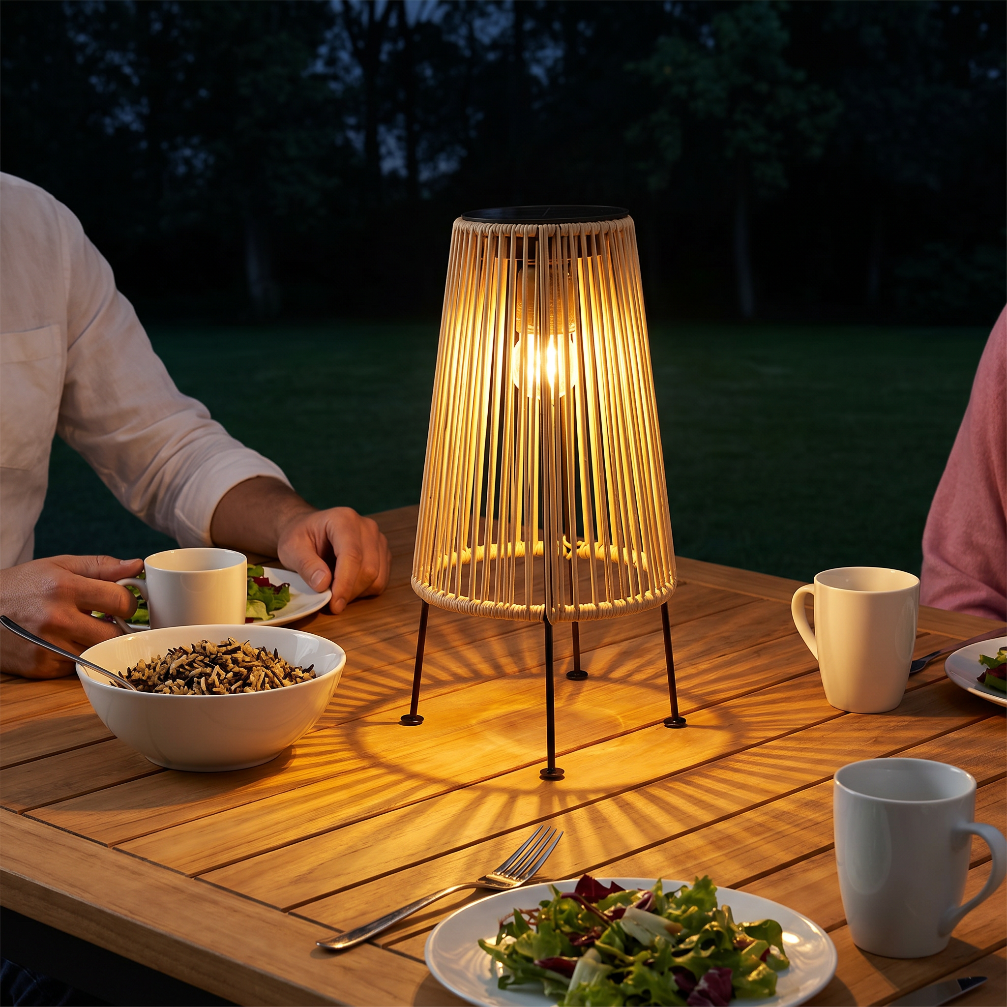 Handwoven rattan geometric solar LED tripod outdoor lantern side profile in natural tan with warm light placed on garden lawn