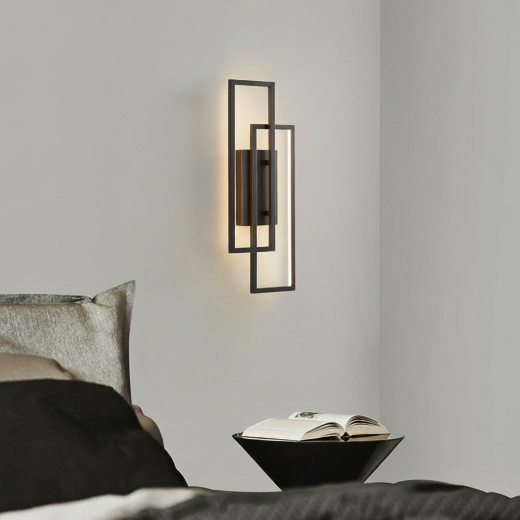 Black geometric LED wall lamp with adjustable color temperature mounted on a bedroom wall above a bedside table with a book.