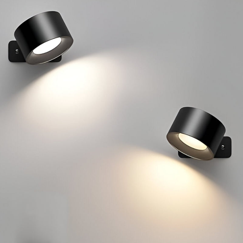 Two black Lumos cordless wall lamps mounted on a light gray wall, casting warm light downwards.