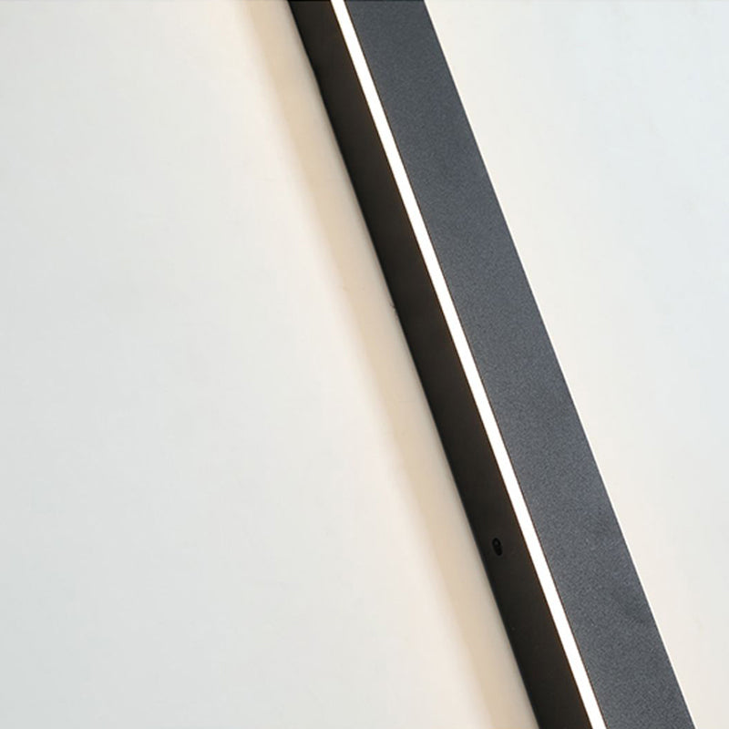 A close-up view of the Luna Edge IP65 linear LED wall light, featuring a black metal finish and an illuminated white light strip, with a visible sensor on the side, mounted on a white wall.