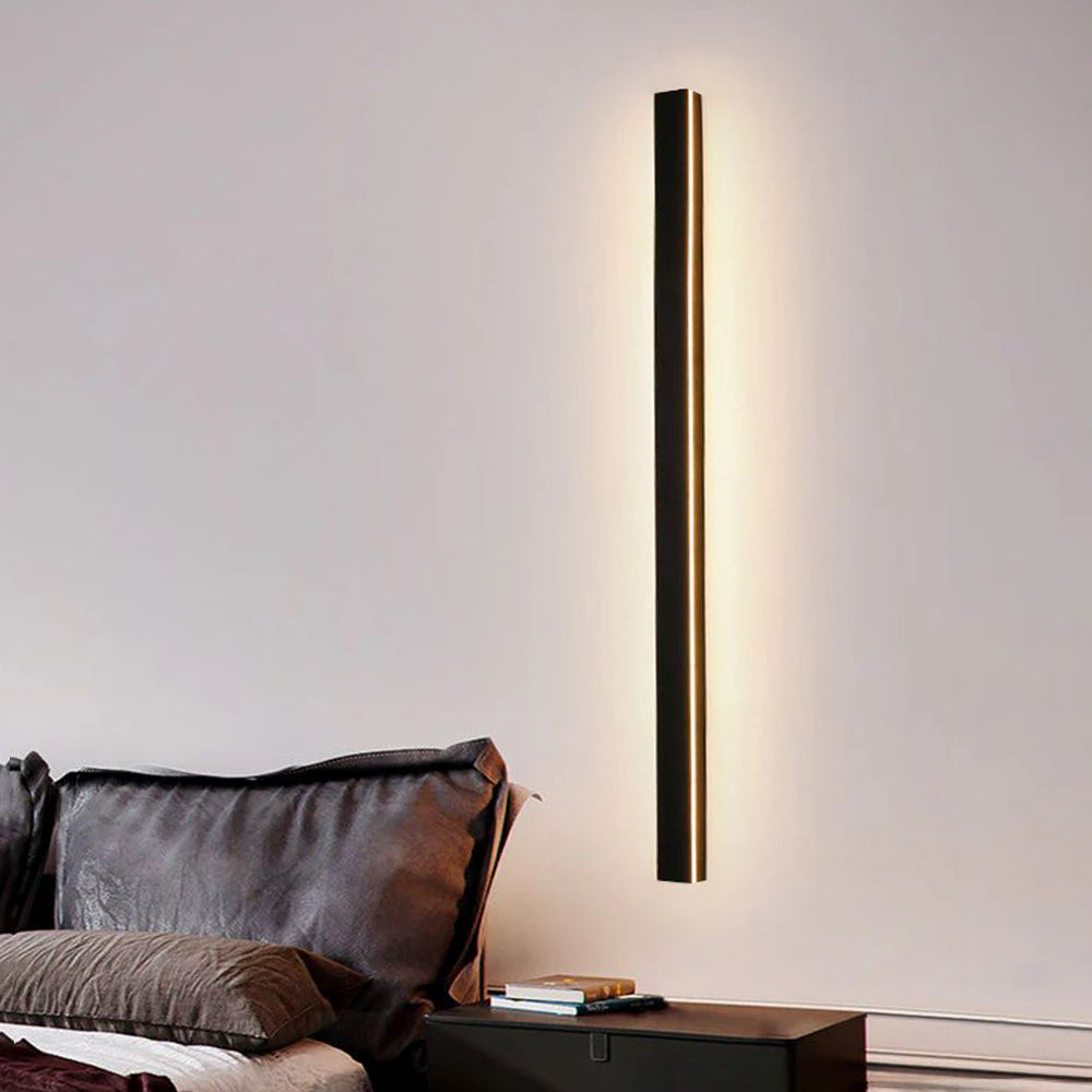 Luna Edge IP65 linear LED wall light in black metal with acrylic finish, emitting warm white light on an interior bedroom wall above a bedside table.