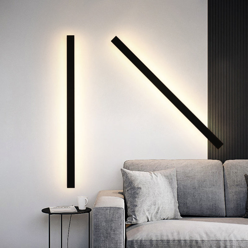Two Luna Edge IP65 linear LED wall lights with black metal and acrylic finish illuminating a modern living room above a grey sofa, one mounted vertically and one diagonally.