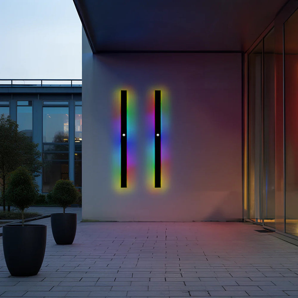Two Luna Edge IP65 linear LED wall lights in black metal with acrylic finish, showcasing vibrant RGB color illumination on a modern building exterior. These weather-resistant outdoor fixtures add dynamic, colorful lighting to contemporary architecture.