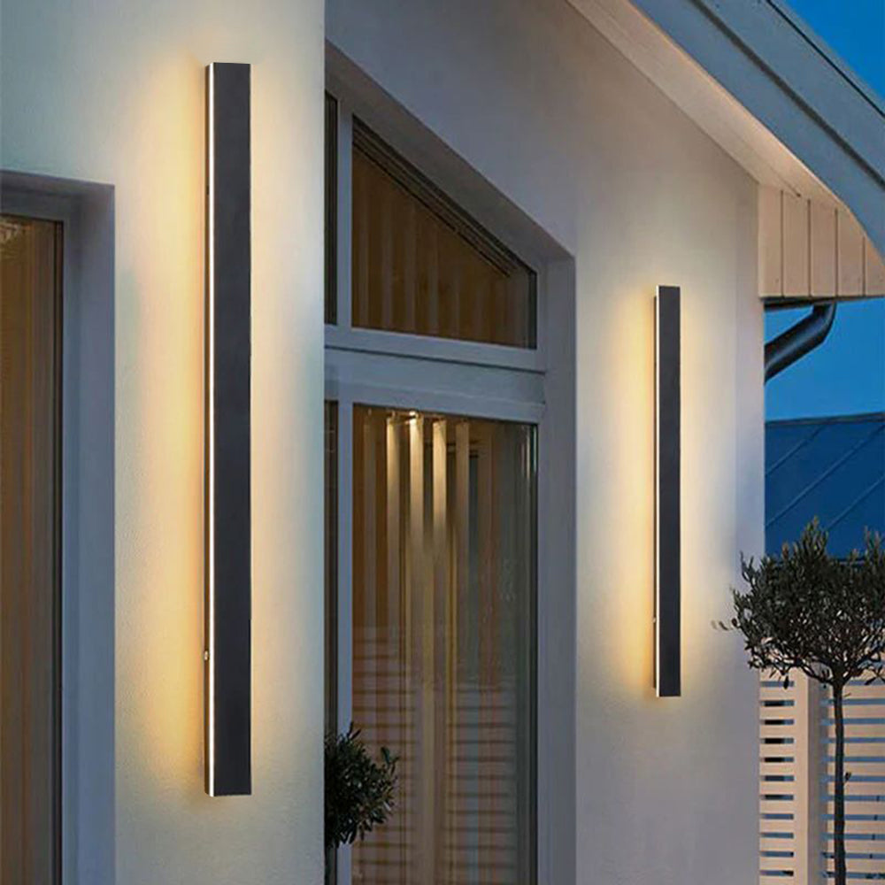 Luna Edge IP65 Linear LED Wall Light in black metal with acrylic finish, featuring two vertical fixtures emitting warm white light on the exterior wall of a modern house. Highlights the sleek design and outdoor illumination capabilities.