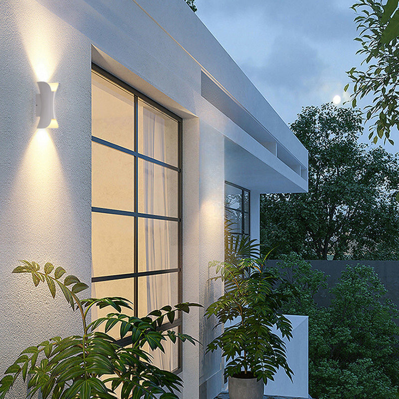 Luna Edge IP65 Linear LED Wall Light Black Metal with Acrylic Finish, showing a white curved wall light with up and down illumination, mounted on a white exterior wall next to a window at dusk. Green plants are in the foreground, highlighting its outdoor application.
