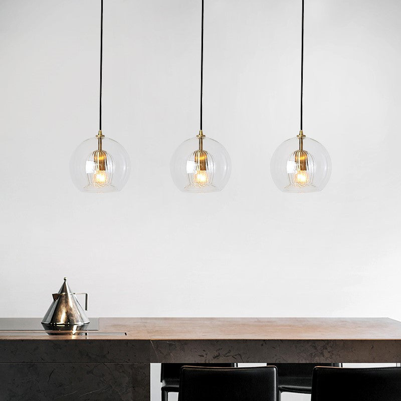 Three Lustre Aura LED pendant lights in clear glass with warm light, suspended over a sleek dark modern dining table, highlighting their contemporary design and adjustable height feature.