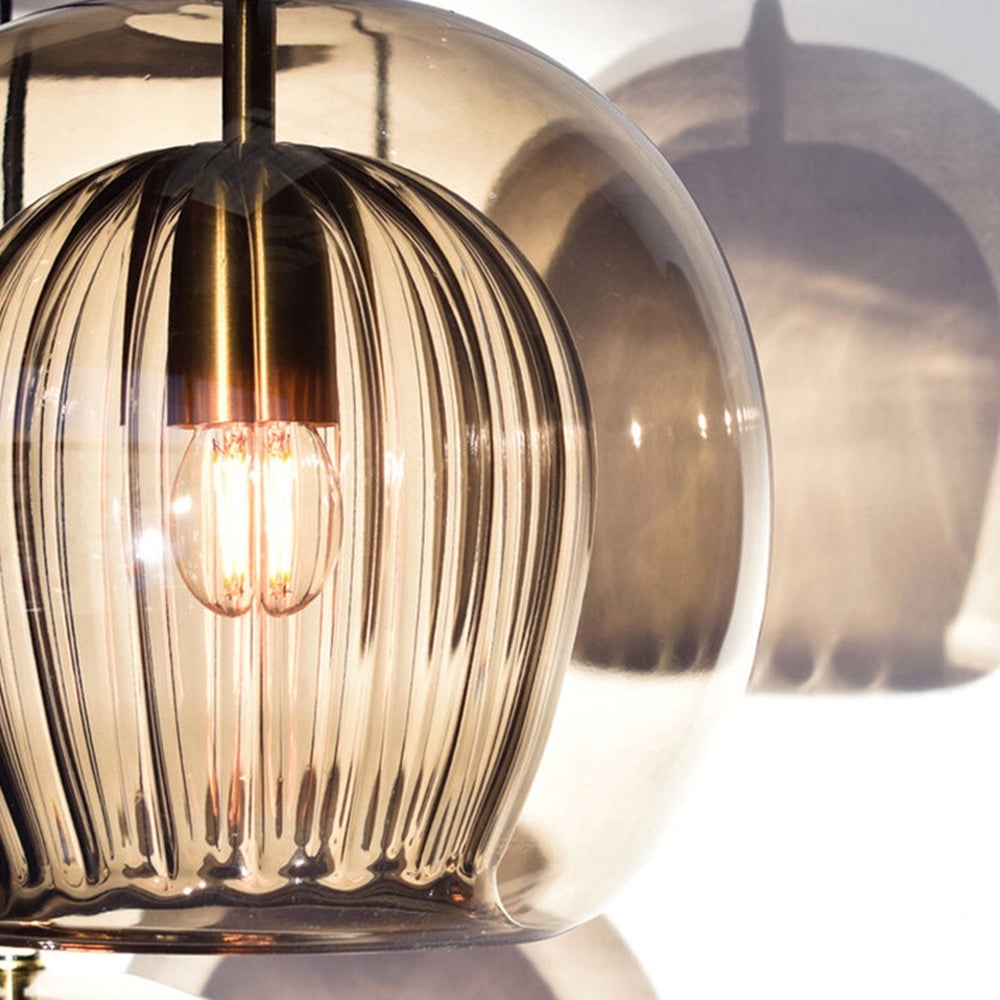 Close-up view of the Lustre Aura LED pendant light in amber glass, highlighting the ribbed inner shade, smooth outer globe, and warm light bulb. The modern fixture casts an elegant shadow, showcasing its unique design.