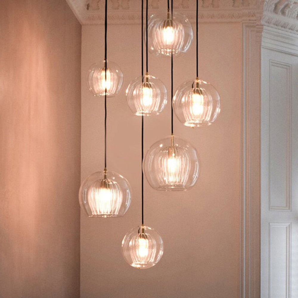 A cluster of Lustre Aura LED pendant lights with clear amber glass and ribbed diffusers, emitting a warm glow, hanging at varying adjustable heights in a modern room setting.
