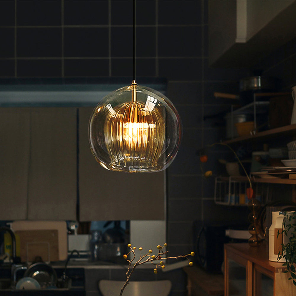 A single Lustre Aura LED pendant light with clear amber glass and a ribbed diffuser, emitting a warm glow, hanging in a contemporary kitchen setting.
