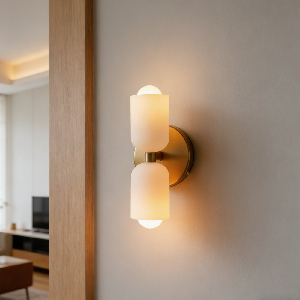 Luxe Parisian Glow LED wall sconce with gold iron finish and two frosted white glass shades, illuminated with a warm glow, mounted on a light gray wall in a modern living room.