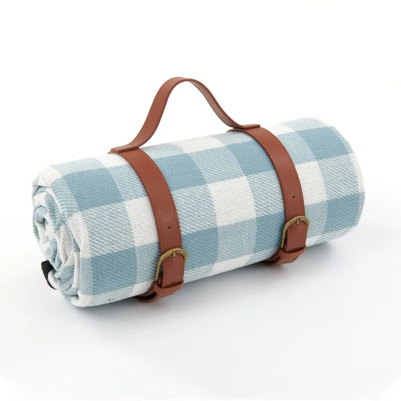 Meadow Escape Waterproof Outdoor Blanket rolled up, featuring a serene light blue and white gingham pattern with brown adjustable faux leather straps and handle. Ideal for beach trips, picnics, and outdoor relaxation.