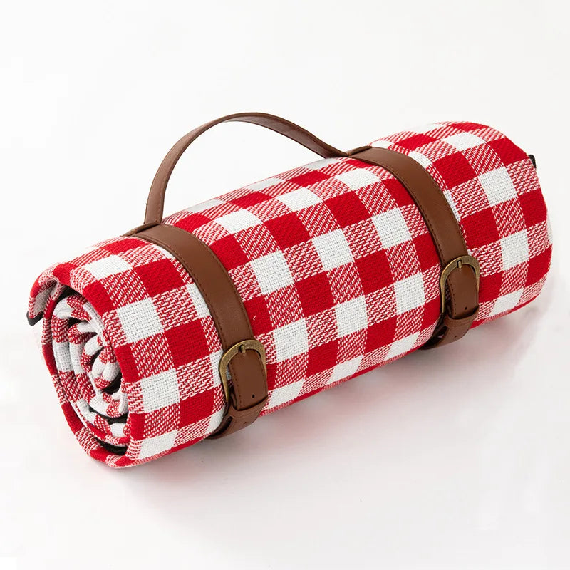 Meadow Escape Waterproof Outdoor Blanket rolled up, featuring a classic red and white gingham pattern with brown adjustable faux leather straps and handle. Perfect for picnics, camping, and outdoor adventures.