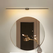 Vestra Minimalist Linear Rechargeable Wall Lamp in black, mounted above a round mirror with a vase of white flowers reflecting a doorway. The lamp emits a warm LED light.