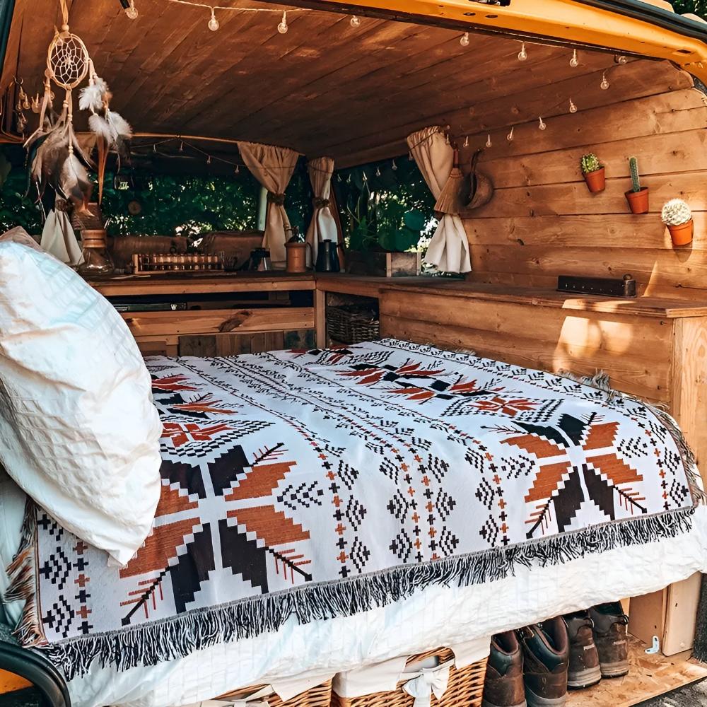 Nomad Oasis picnic blanket with Moroccan boho pattern used as a bedspread inside a cozy wooden camper van, showcasing its versatile use.