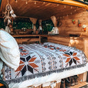 Nomad Oasis picnic blanket with Moroccan boho pattern used as a bedspread inside a cozy wooden camper van, showcasing its versatile use.
