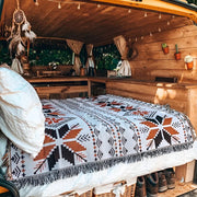 Nomad Oasis picnic blanket with Moroccan boho pattern used as a bedspread inside a cozy wooden camper van, showcasing its versatile use.