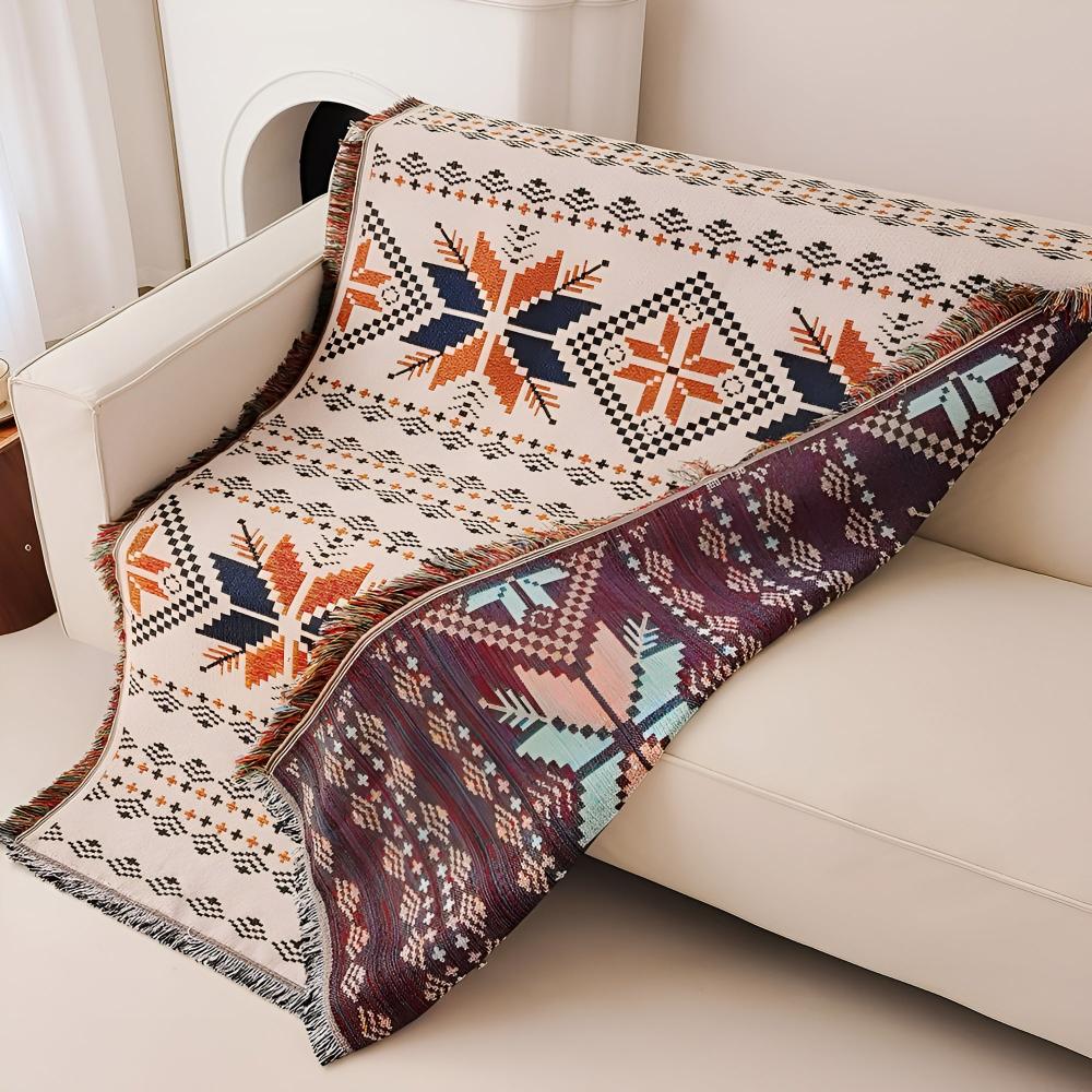 Nomad Oasis picnic blanket with Moroccan boho pattern draped over a white sofa, revealing its reversible side with a distinct pattern and color scheme, offering versatile styling options.