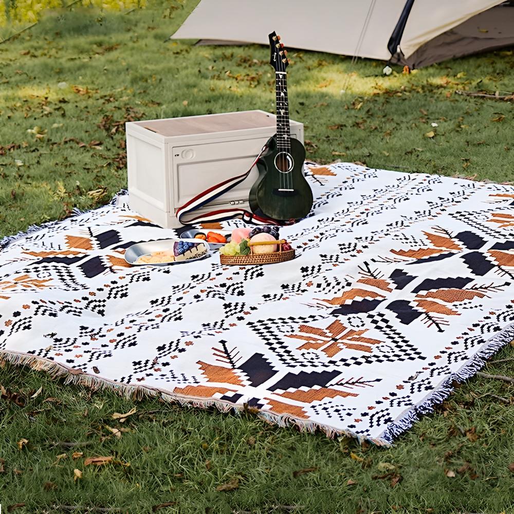 Nomad Oasis picnic blanket with Moroccan boho pattern spread on green grass, featuring a ukulele, a white cooler, and a basket of snacks, perfect for a relaxing outdoor gathering.
