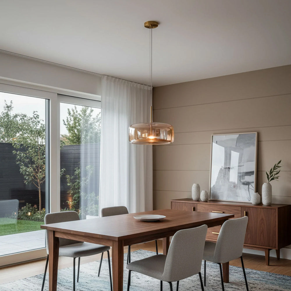 Nordic Glow Smoked Glass LED Pendant Light in amber, suspended above a dark wood dining table with grey chairs, in a dining room with a garden view. Complements a modern, industrial style interior.