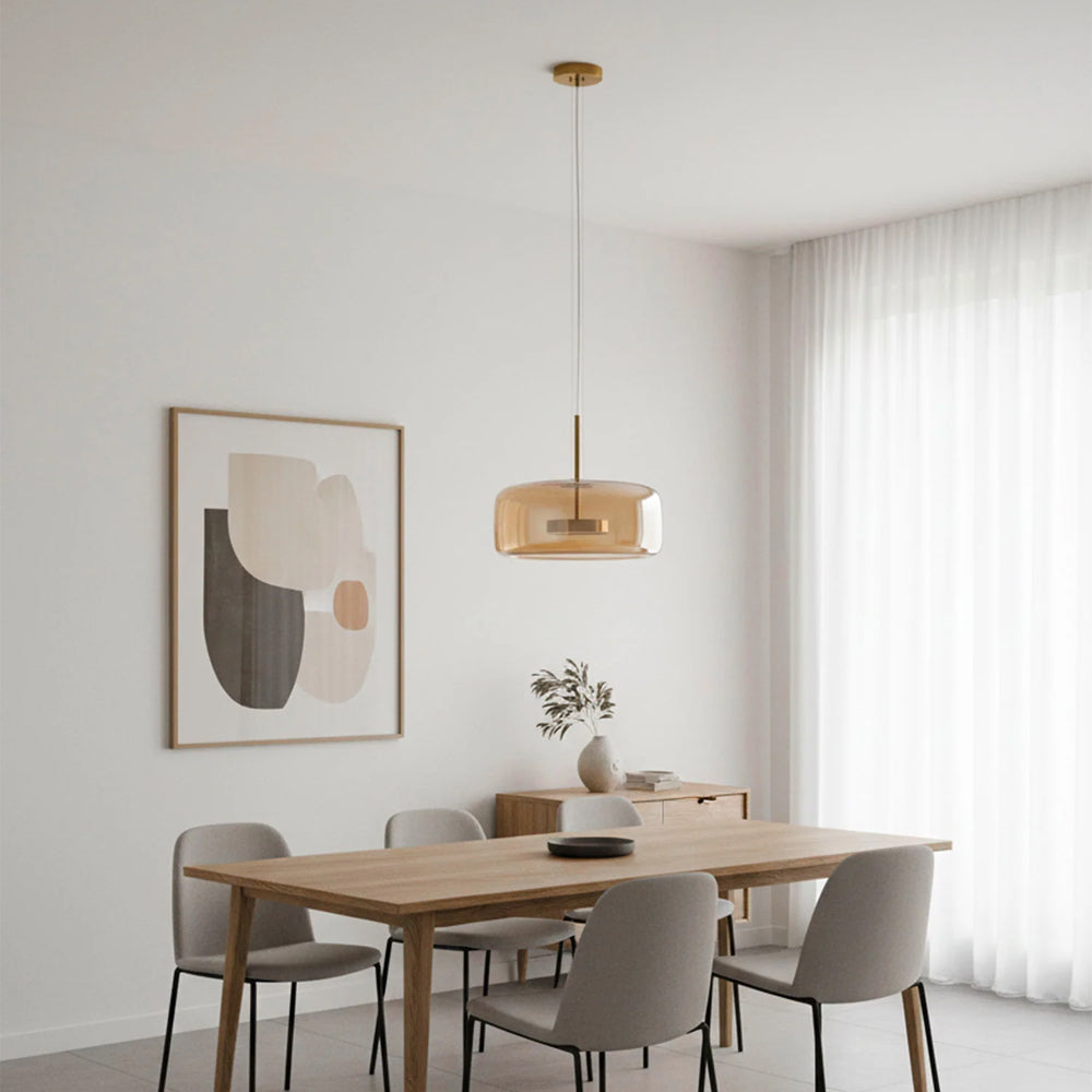 Nordic Glow Smoked Glass LED Pendant Light in amber, featured in a bright, minimalist dining room with a light wood table, grey chairs, and abstract wall art. A modern and ambient pendant light.